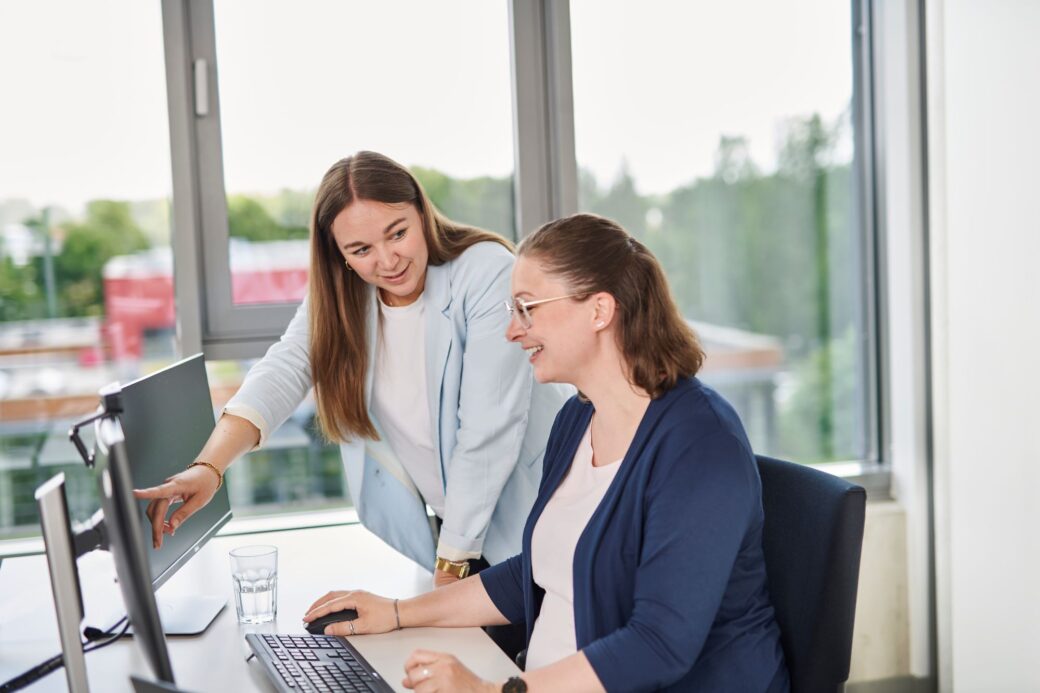 An employee explains something to another employee on the computer as part of onboarding