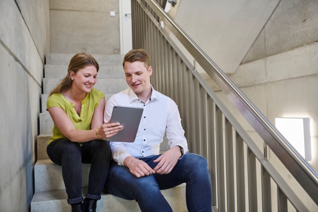 A colleague supports a new colleague during onboarding while showing him something on a tablet